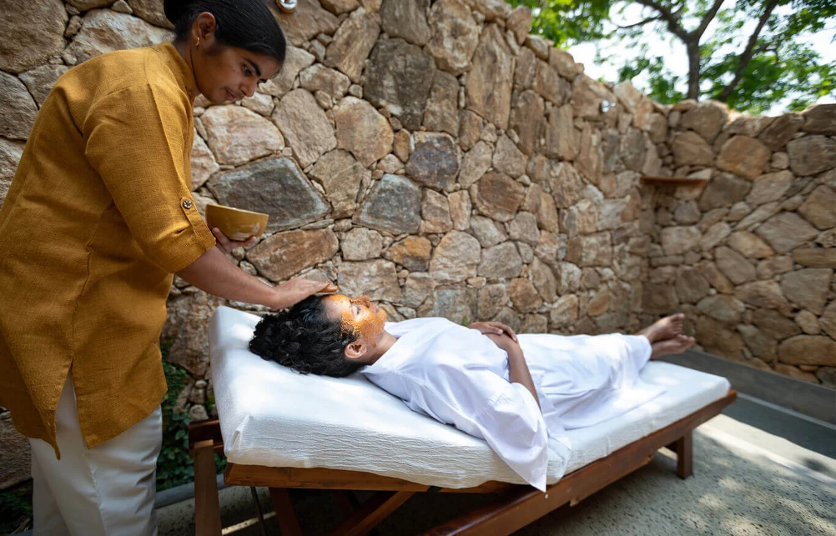 Guest receiving mud therapy treatment in natural outdoor setting.